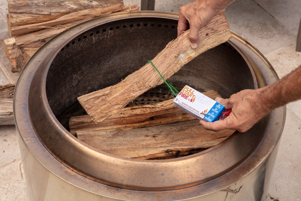Man placing Pull Start Fire firestarter and wood into a stainless steel fire pit