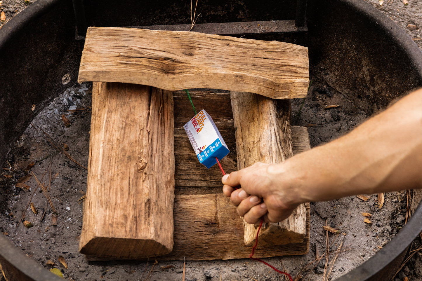 
                  
                    Hand pulling the string to activate Pull Start Fire firestarter in a campfire
                  
                