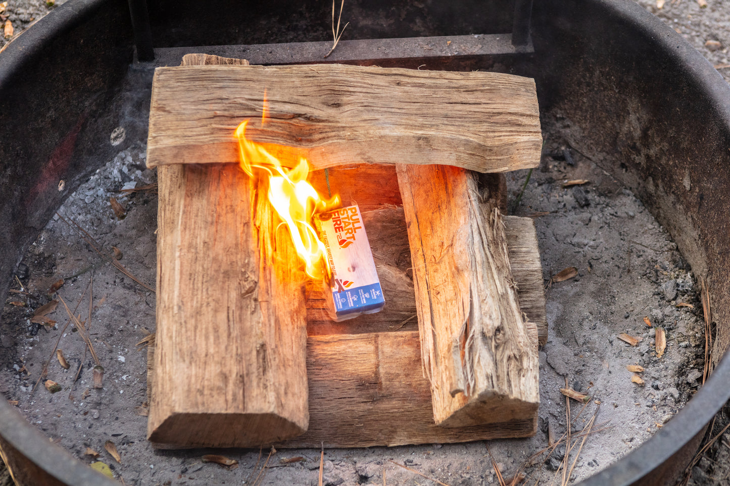 
                  
                    Pull Start Fire starter igniting a campfire with wet wood in a fire pit
                  
                